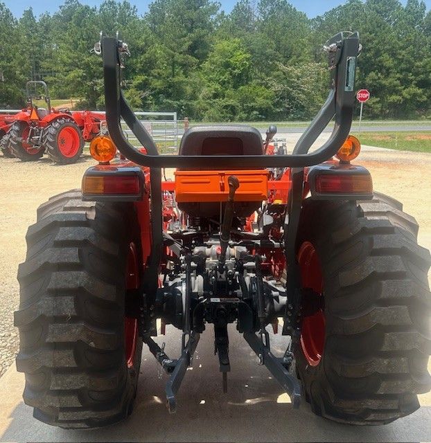 Rear view of an orange tractor with black safety bars and large treaded tires outdoors.