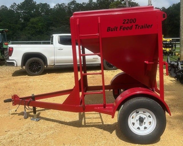 Red 2200 bulk feed trailer with ladder and hitch, parked near white pickup truck.