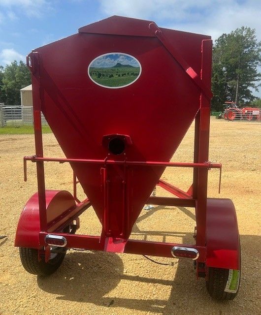 Red farm feed hopper on wheels, with a painted scene, in a rural setting.