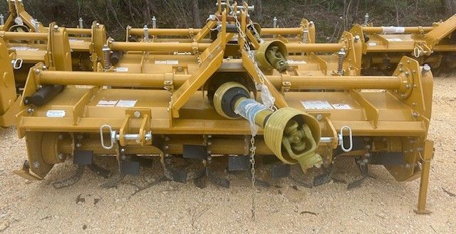 Yellow tractor rotary tiller on dirt, ready to till soil.
