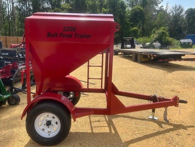 Red 2200 Bull Feed Trailer with a hopper, ladder, and white-rimmed wheels on a sunny day.