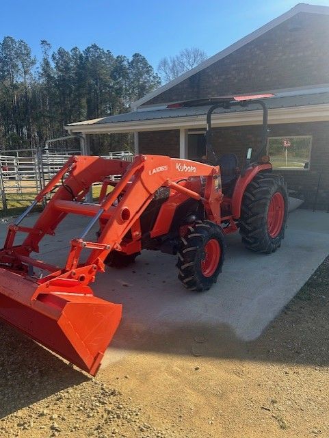 Orange Kubota tractor with a front loader, parked in front of a building.