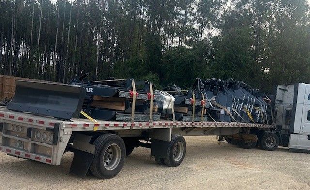Flatbed truck loaded with black metal sheets, secured for transport, in a wooded area.