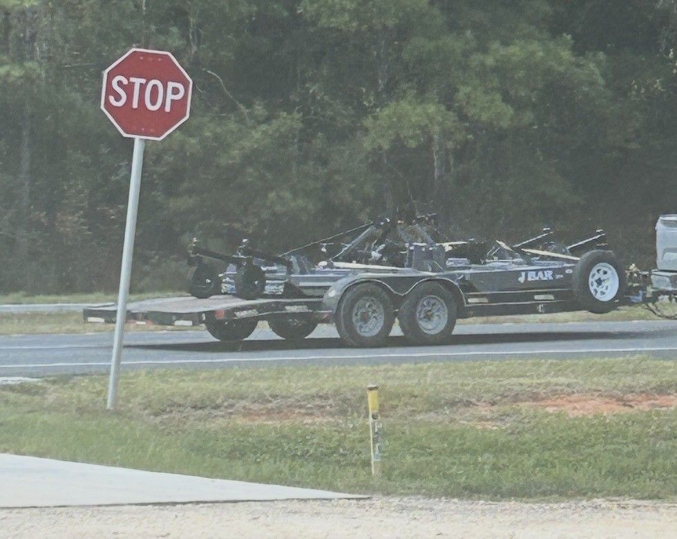 A trailer with a car on it drives past a stop sign along a highway.