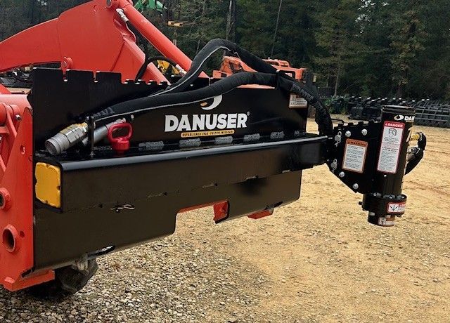 Black Danuser tree shear attachment on an orange tractor in a grassy setting.