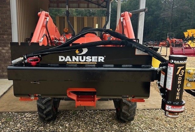 A black Danuser T3 post driver attached to a tractor with orange accents.