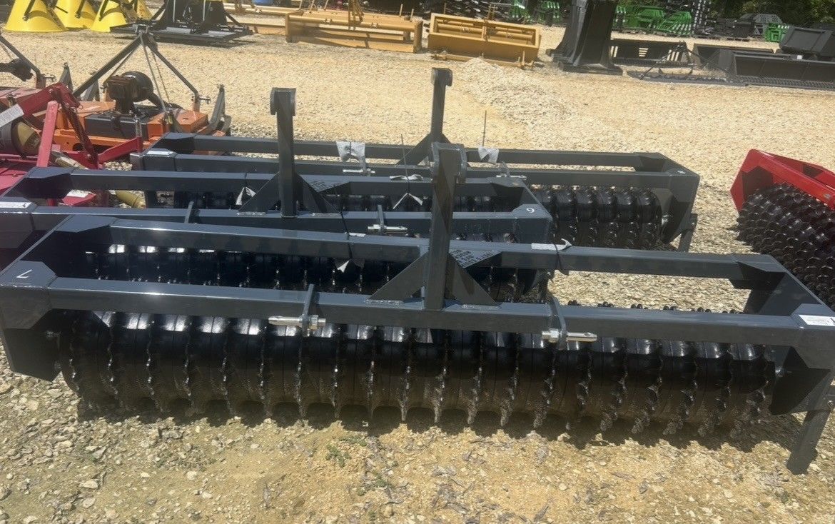 Three dark gray agricultural disc harrows on gravel.