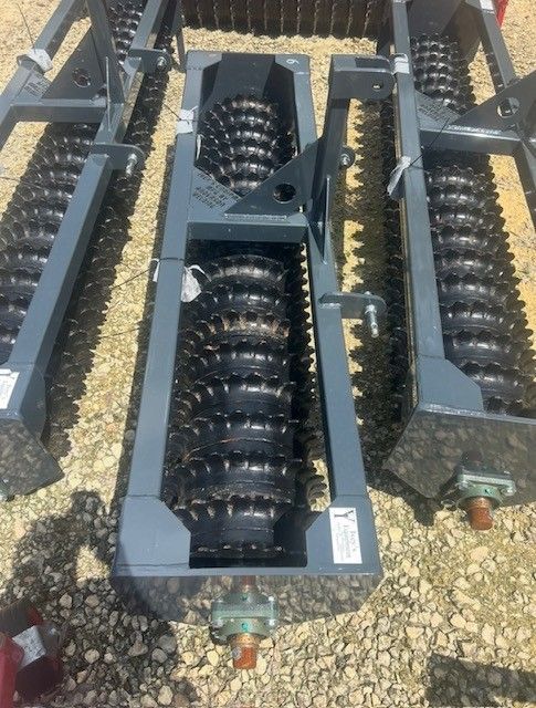Three soil rollers with spiked wheels. Gray metal frames, outdoors on a sunny day.