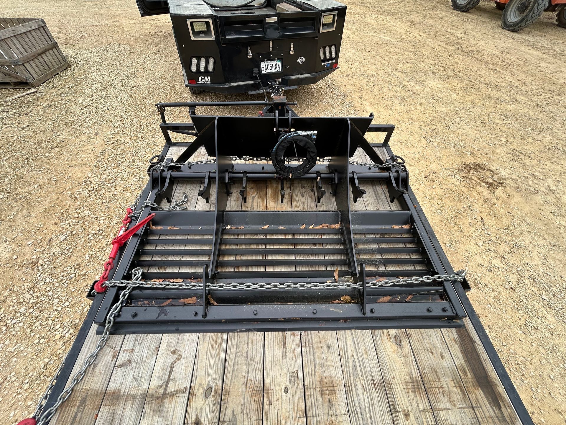 Flatbed trailer with a black land leveler attached, outdoors.