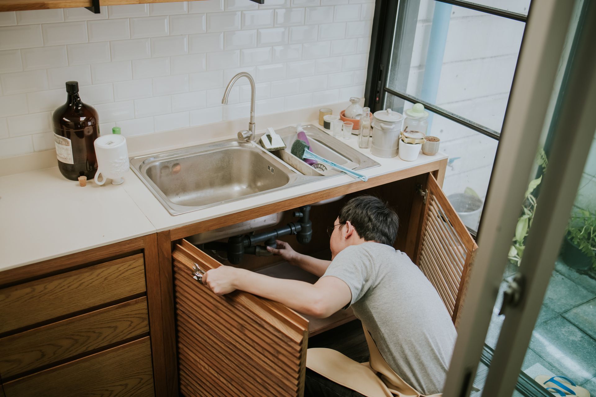 Technician under kitchen sink performing drain cleaning in modern residential home.