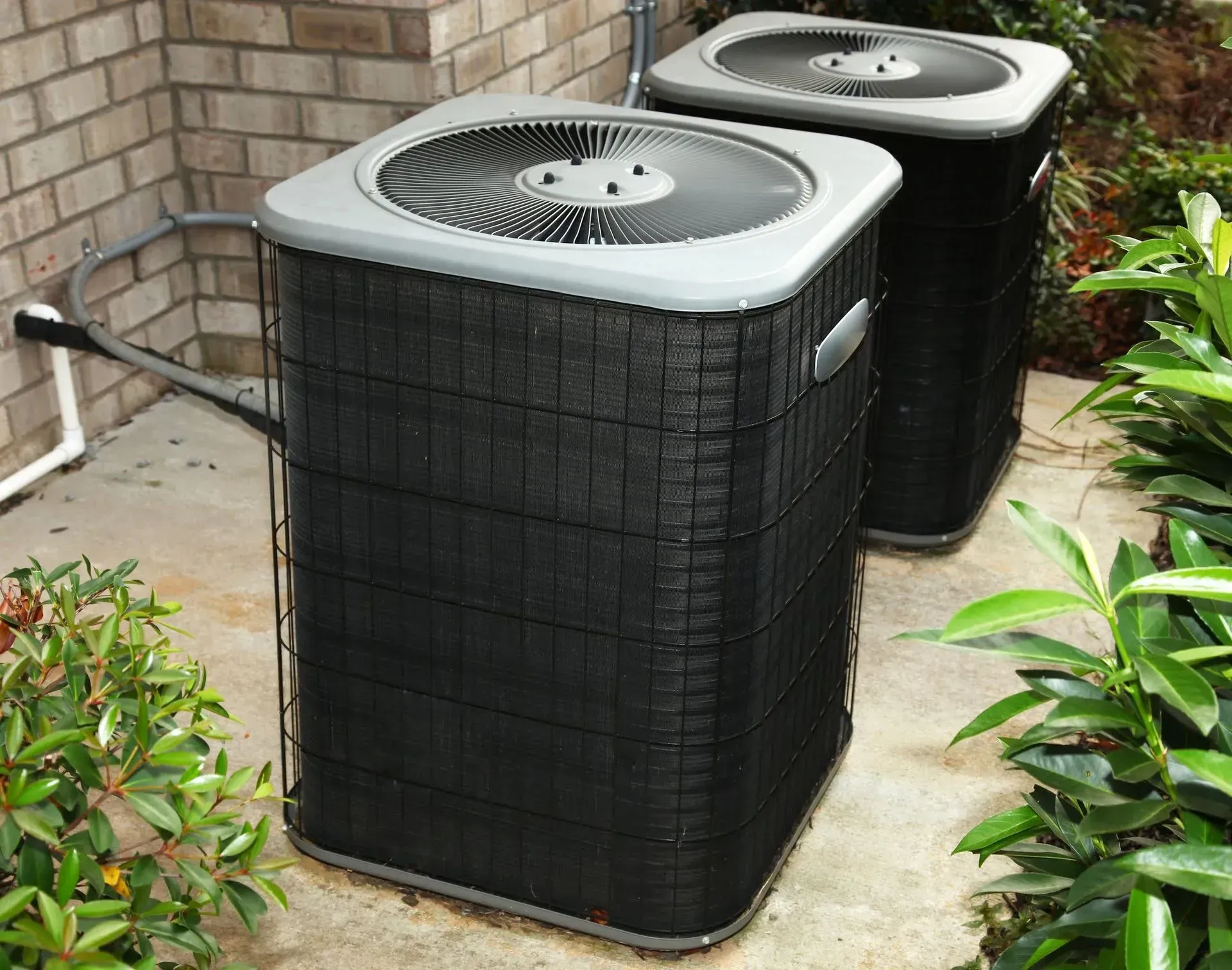 Two air conditioners are sitting on the side of a brick building.