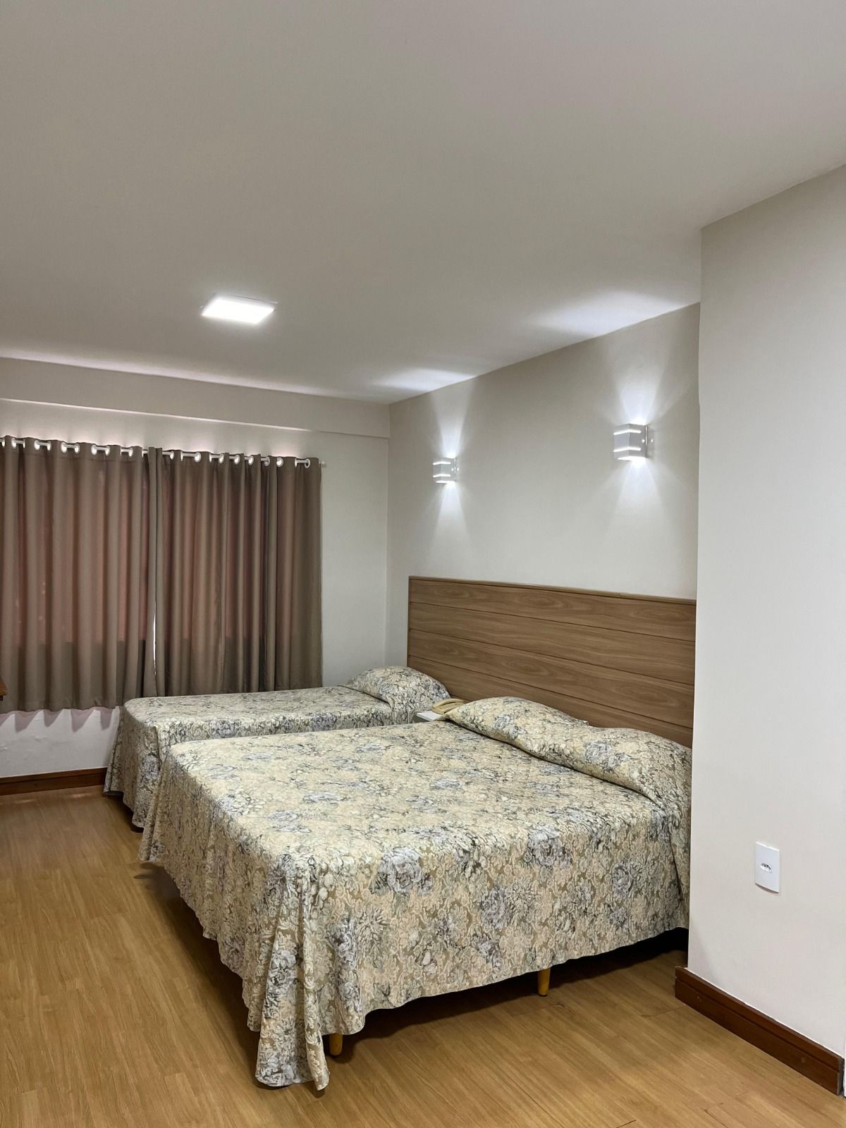 Um quarto de hotel com duas camas cobertas com colchas estampadas com flores, cabeceira de madeira e paredes de cores claras.