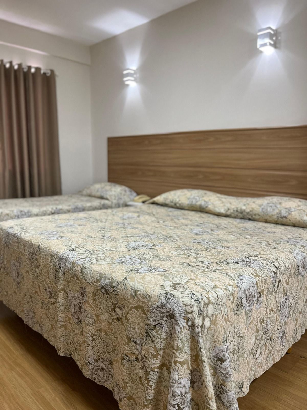 Duas camas em um quarto com colchas estampadas, cabeceira de madeira e arandelas de parede.