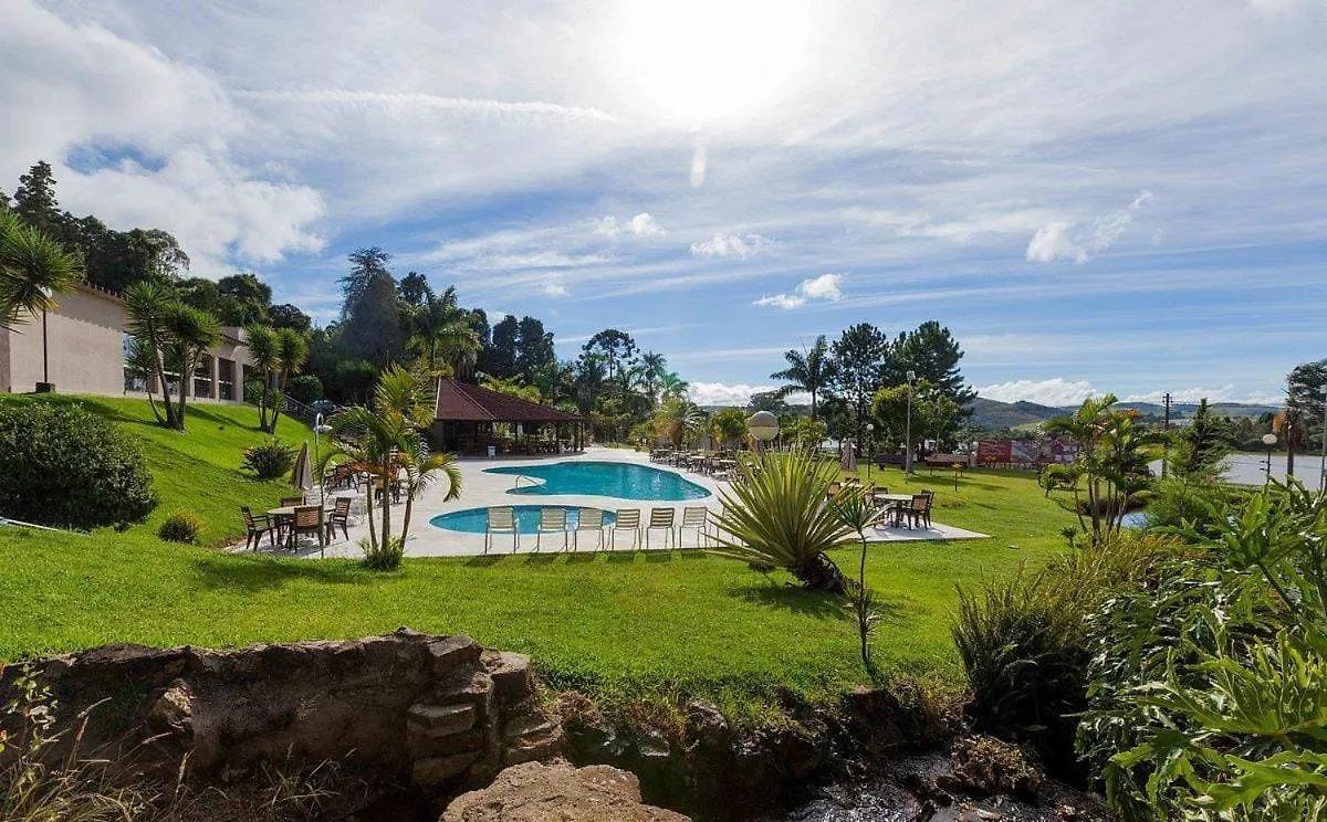 Vista da piscina de um resort com piscina, mesas e área verde sob um céu ensolarado.
