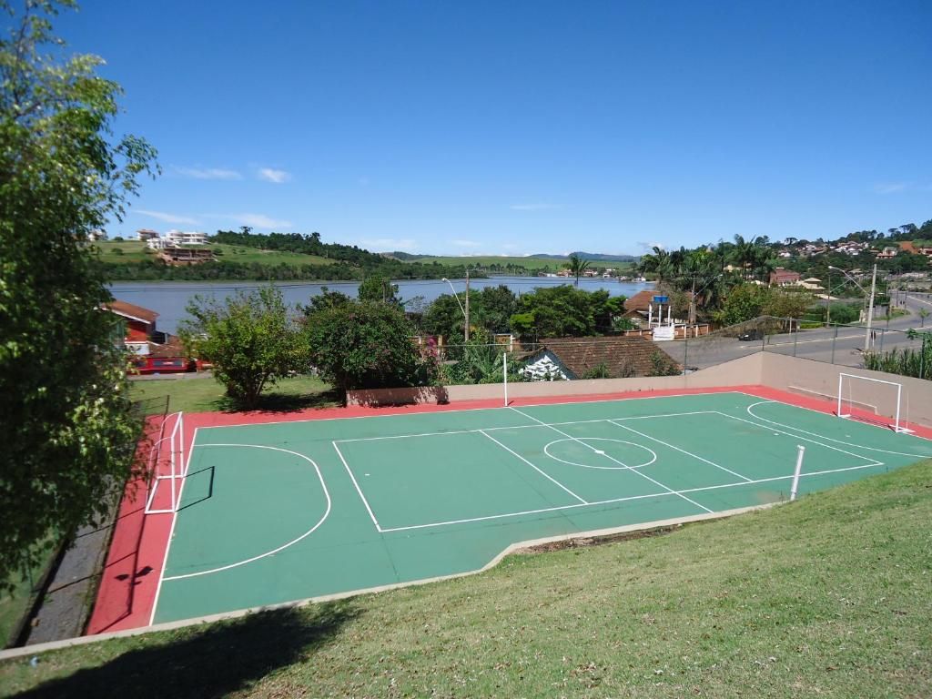 Quadra esportiva verde com marcações, com vista para um lago e para a cidade em um dia ensolarado.