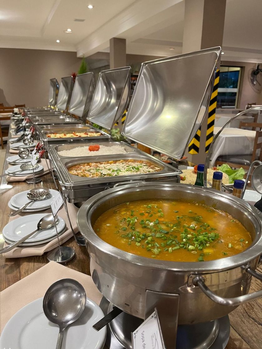 Mesa de bufê com vários pratos; sopa em primeiro plano, bandejas cobertas de comida ao fundo.