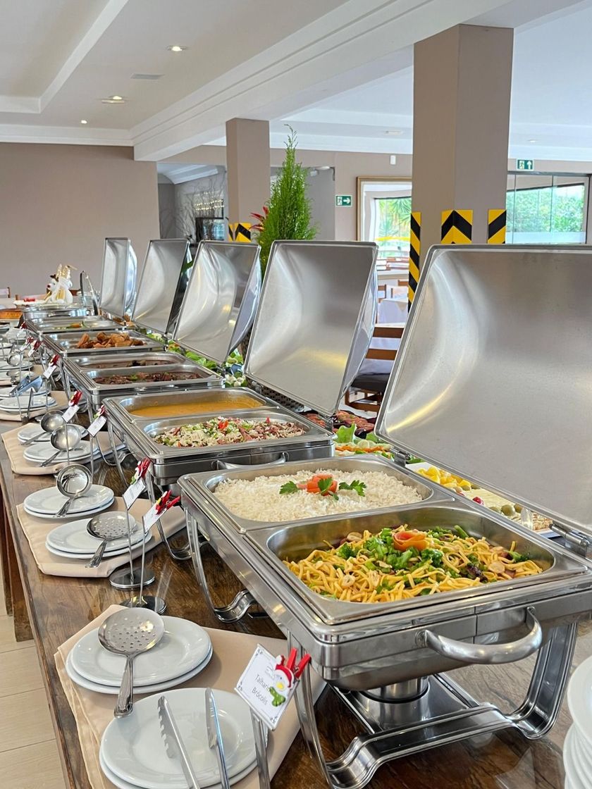 Buffet com pratos variados em travessas de prata, prontos para servir.