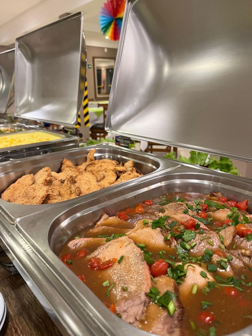 Buffet com pratos variados: frango, carne cozida e legumes, em ambiente bem iluminado.