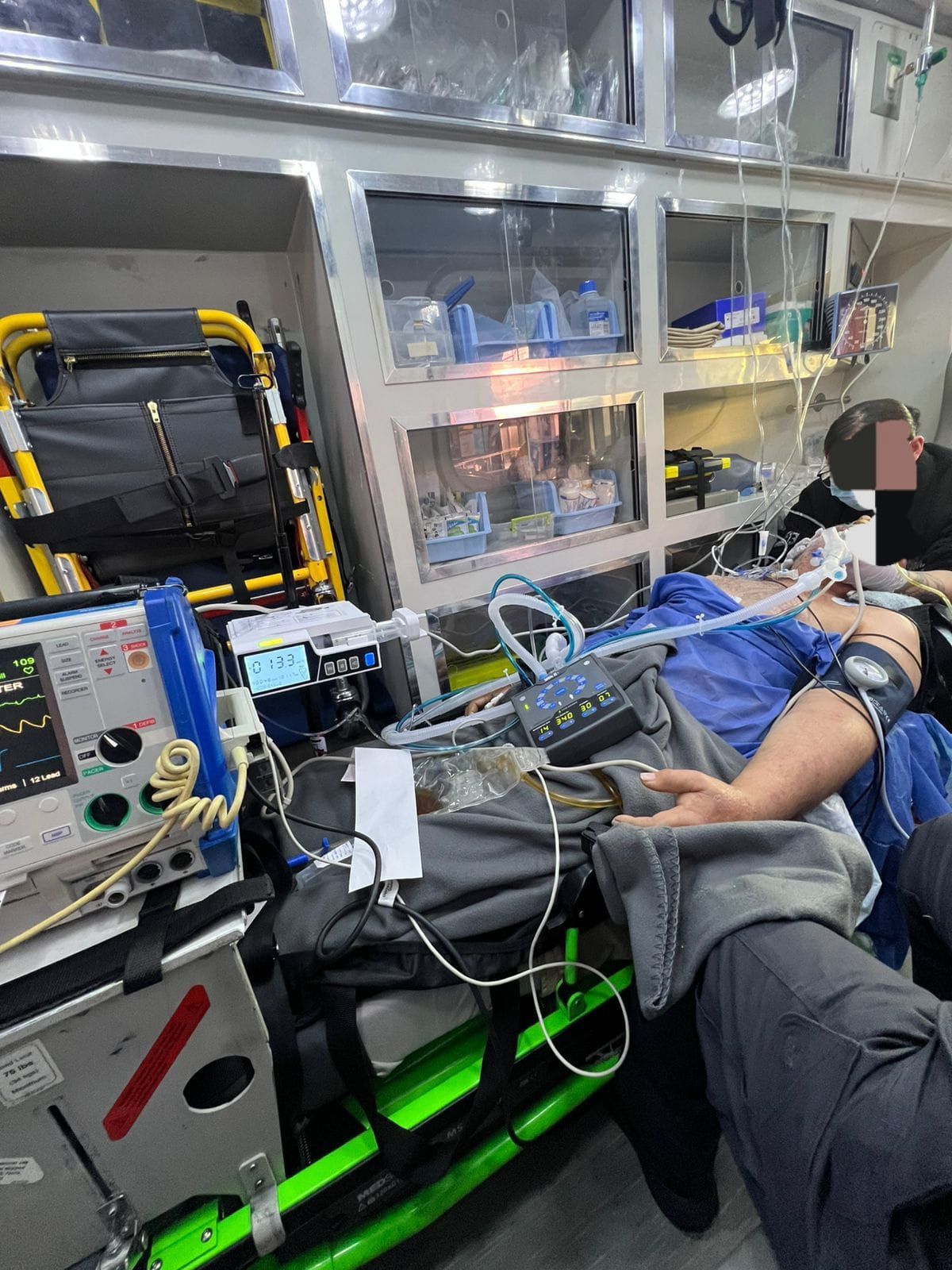 Persona en camilla dentro de ambulancia, conectada a equipo médico.