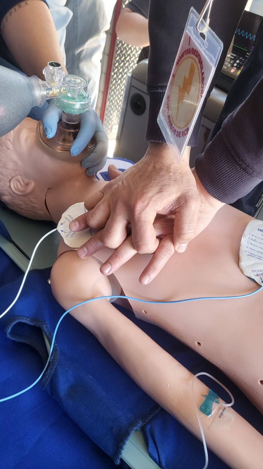 Manos realizando RCP en un maniquí de entrenamiento; otra persona utiliza una máscara con bolsa y válvula.