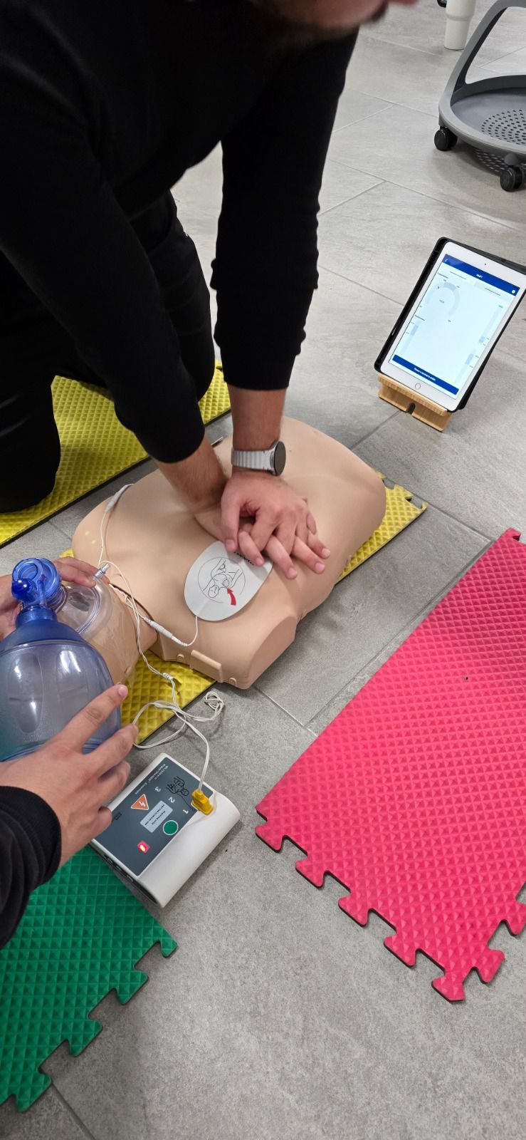 Persona realizando RCP en un maniquí durante una sesión de entrenamiento. Se ve una tableta.