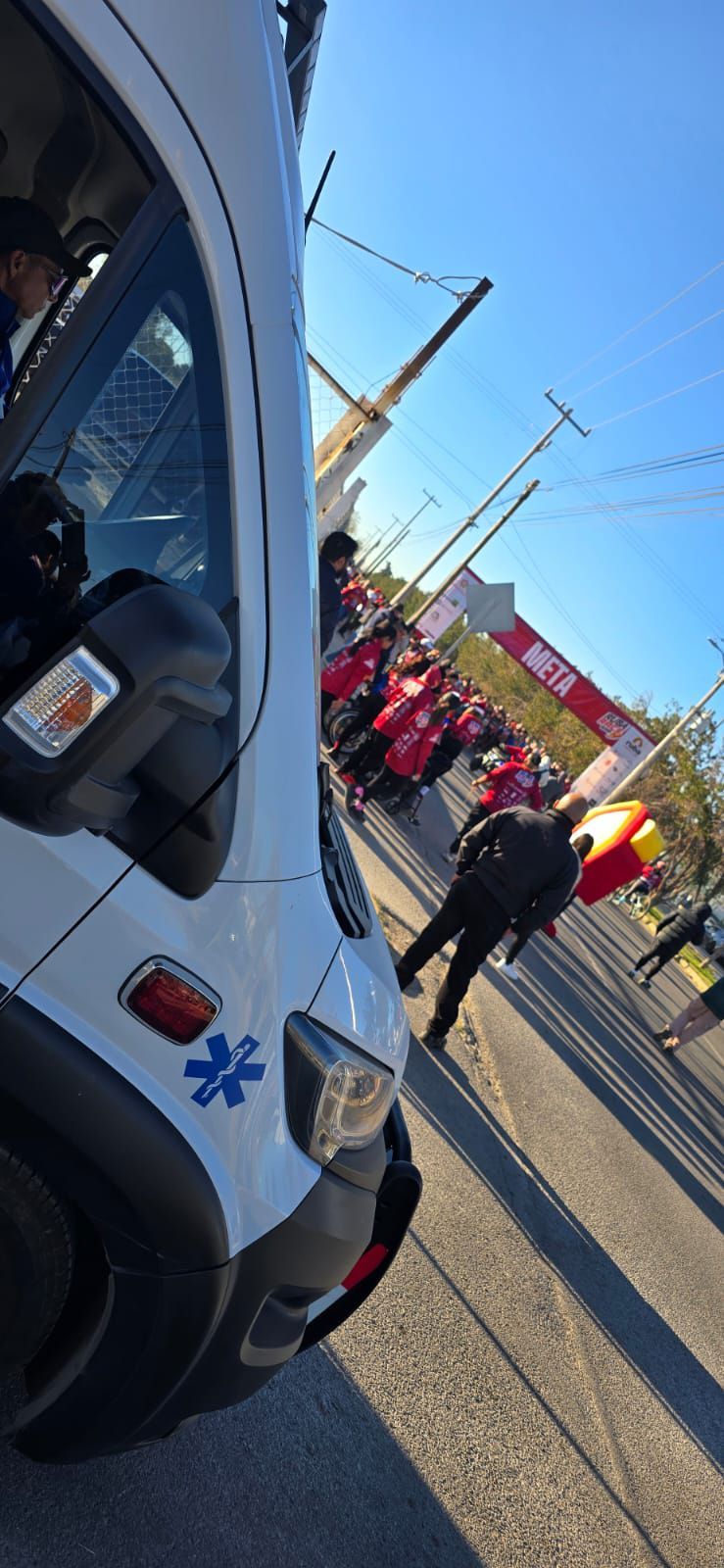 Una ambulancia en una calle con un grupo de personas, bajo un cielo azul.