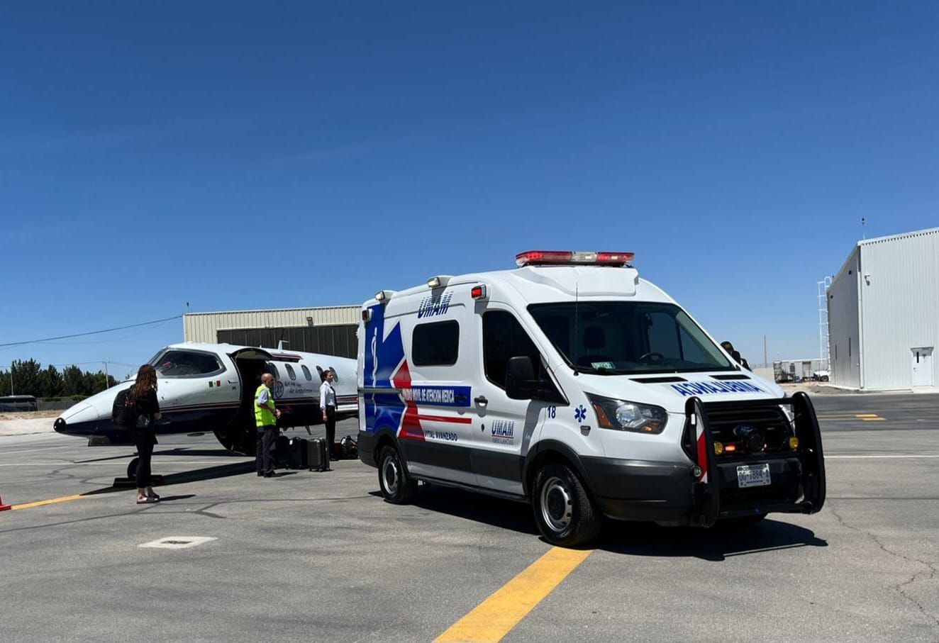 Una ambulancia junto a un avión privado en una pista; personal médico cerca del avión en un día soleado.