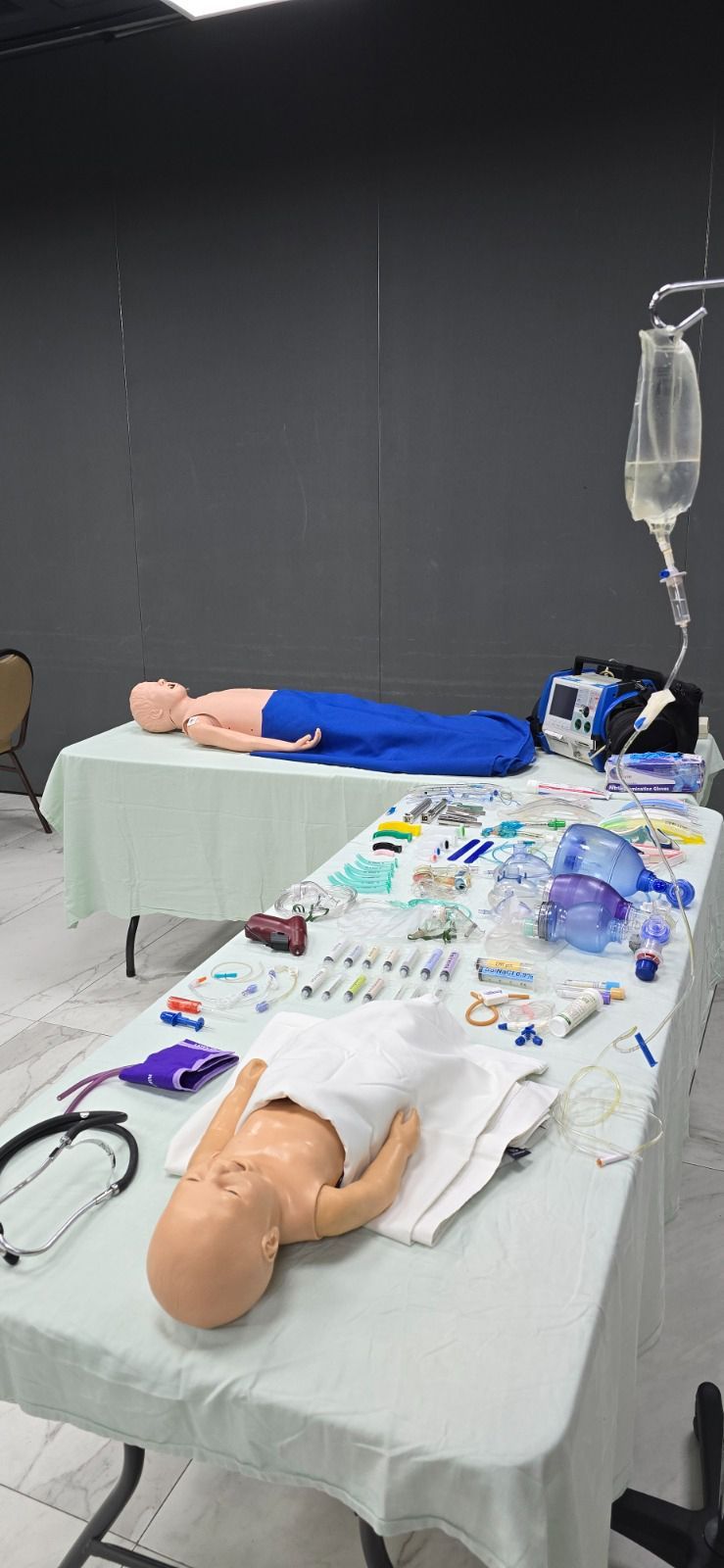 Una sala de capacitación con maniquíes médicos y suministros sobre mesas. Una mesa tiene un maniquí de bebé.