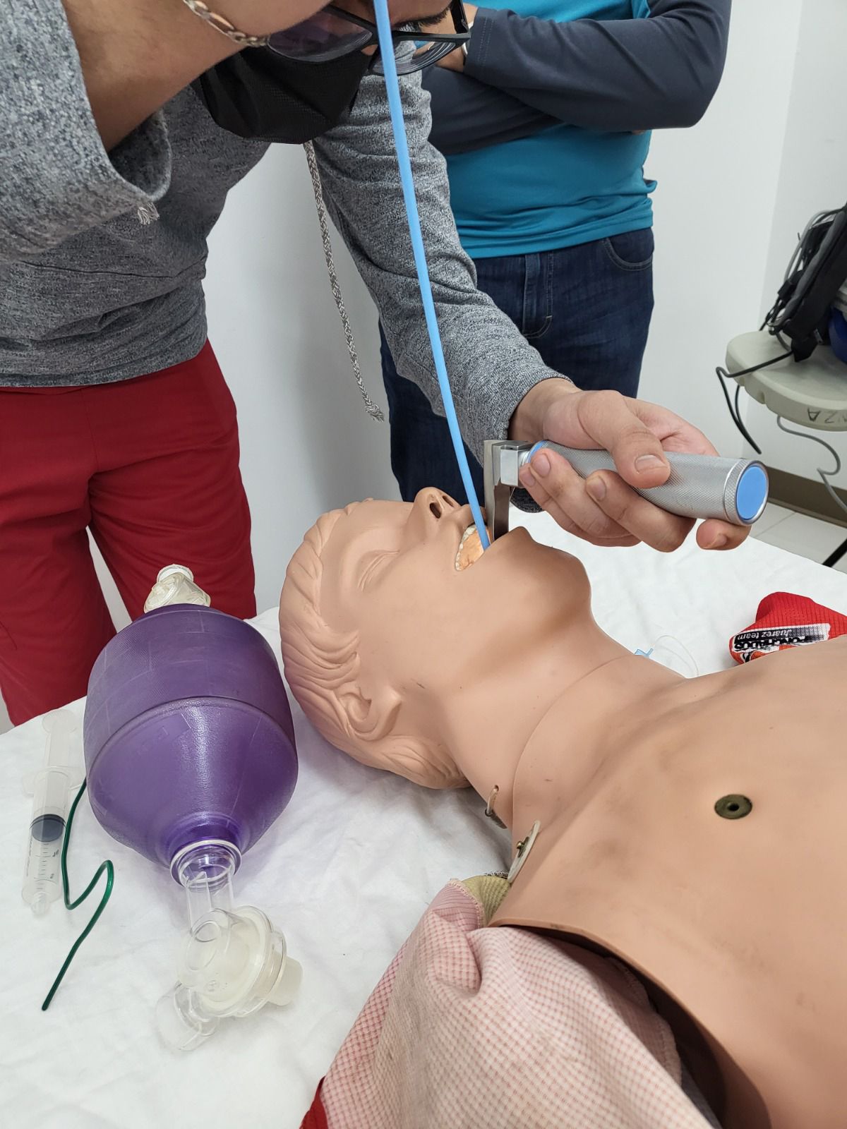 Una persona practica la intubación en un maniquí de entrenamiento médico. Cerca hay una mascarilla con bolsa-válvula.