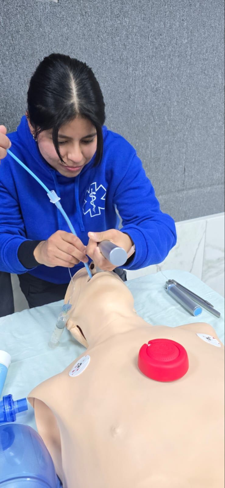 Una persona con una sudadera azul utiliza una jeringa para trabajar en un maniquí de entrenamiento médico.