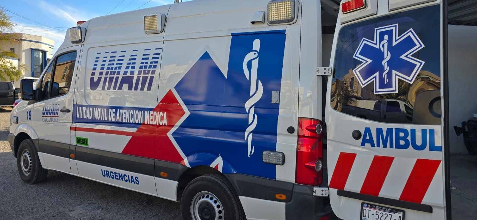 Vista lateral de una ambulancia blanca con detalles azules y rojos, estacionada al aire libre.