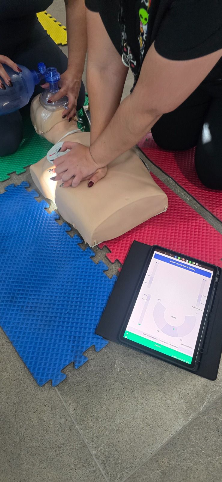 Personas practicando RCP en un maniquí de entrenamiento, usando un iPad para monitorear el progreso.