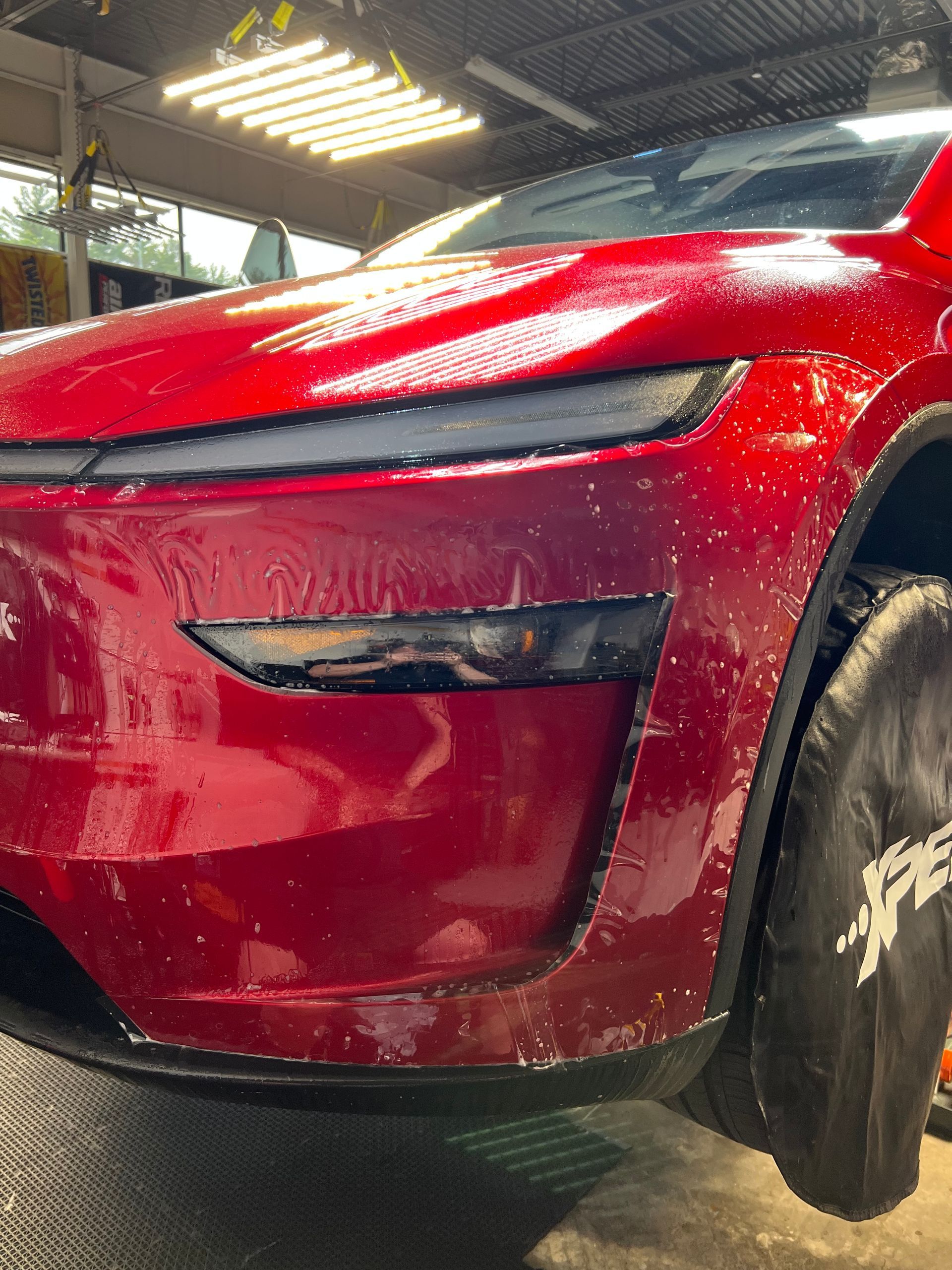 Red car being detailed; close-up of front bumper and headlight, with soap suds.