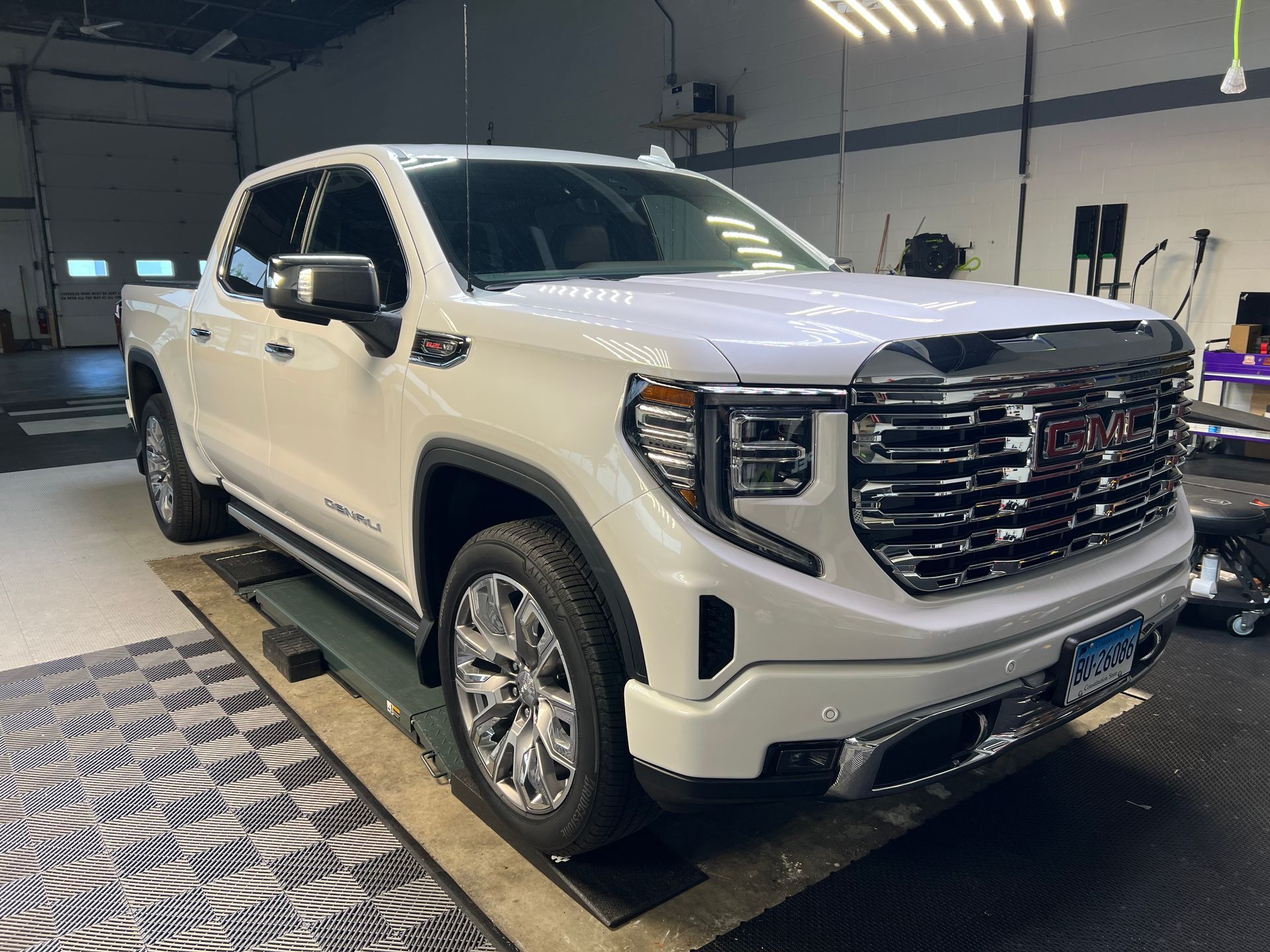 White GMC Sierra pickup truck in a garage, chrome accents, large tires.