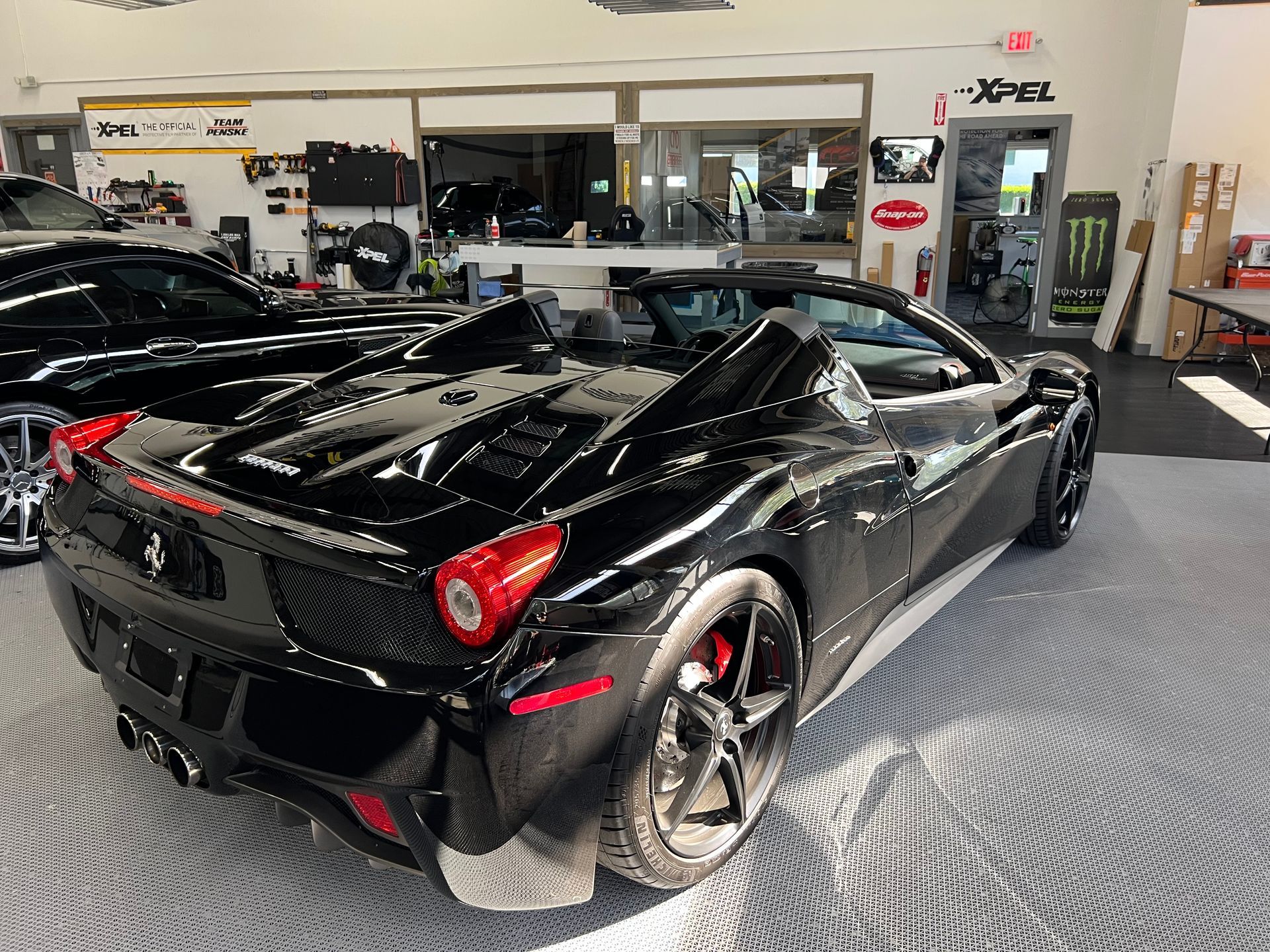 Black Ferrari convertible inside a garage with red brake calipers, white stripe, and glossy finish.
