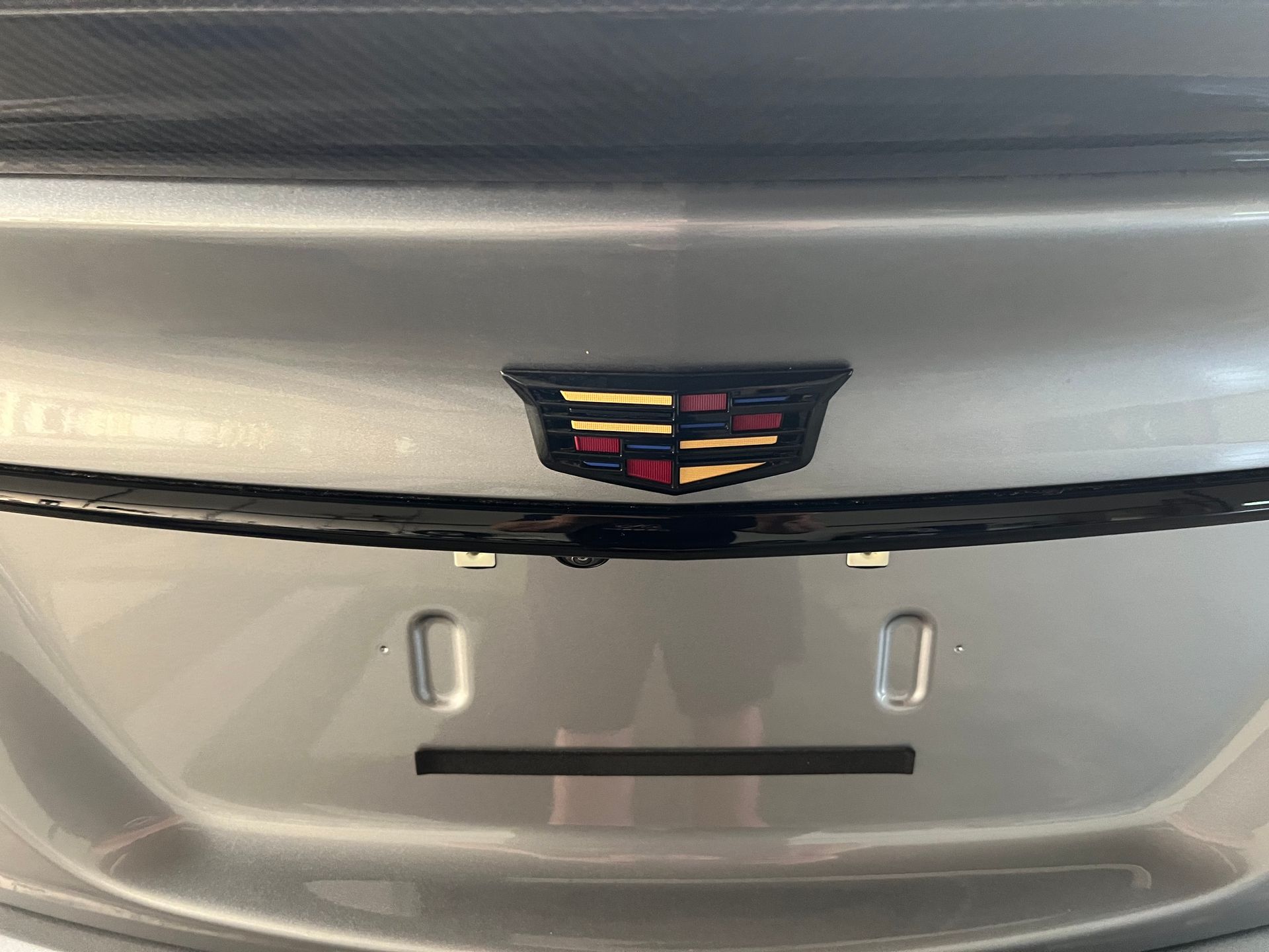 Silver Cadillac trunk with black and gold emblem, license plate area, and camera.