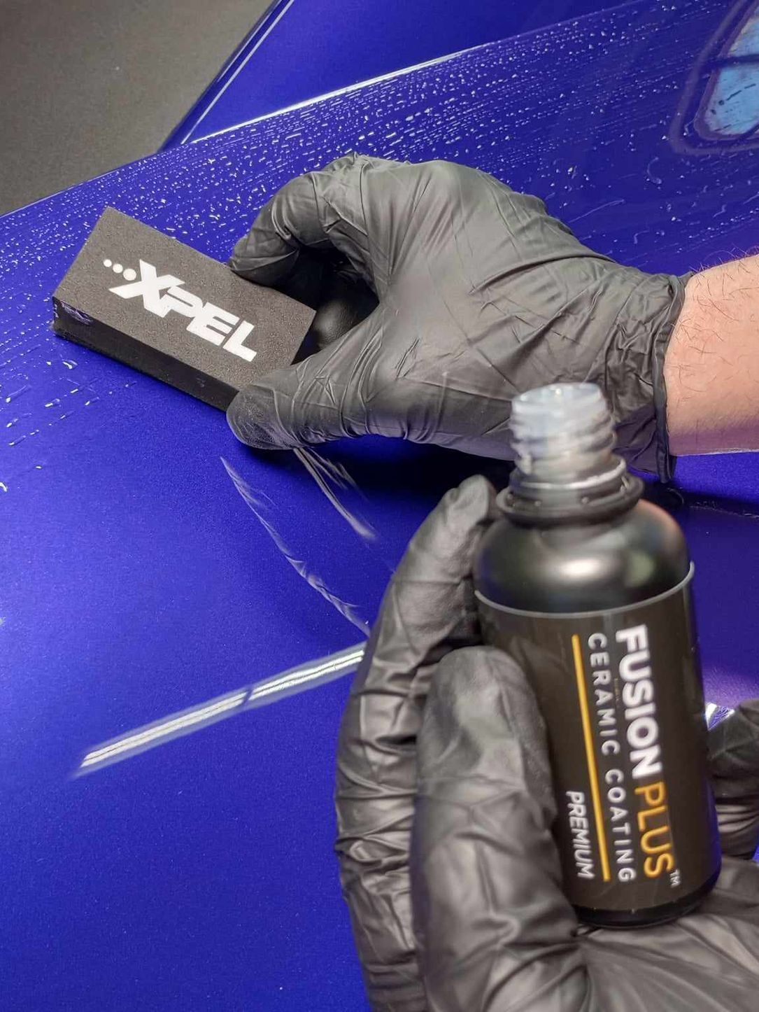 A person wearing black gloves is polishing the hood of a red car.