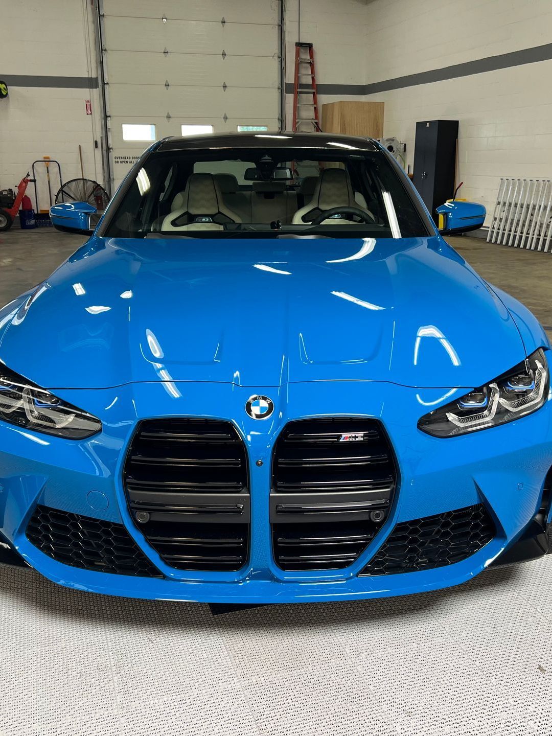 A person is using a blue squeegee to remove plastic from the hood of a car