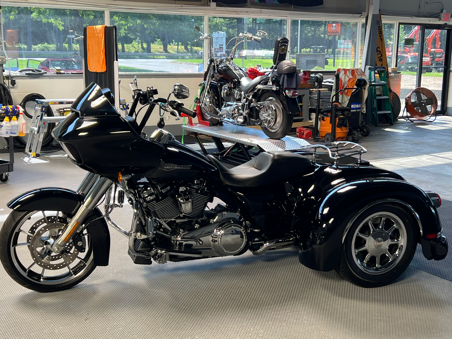 Black Harley-Davidson trike in a showroom, with a motorcycle in the background.