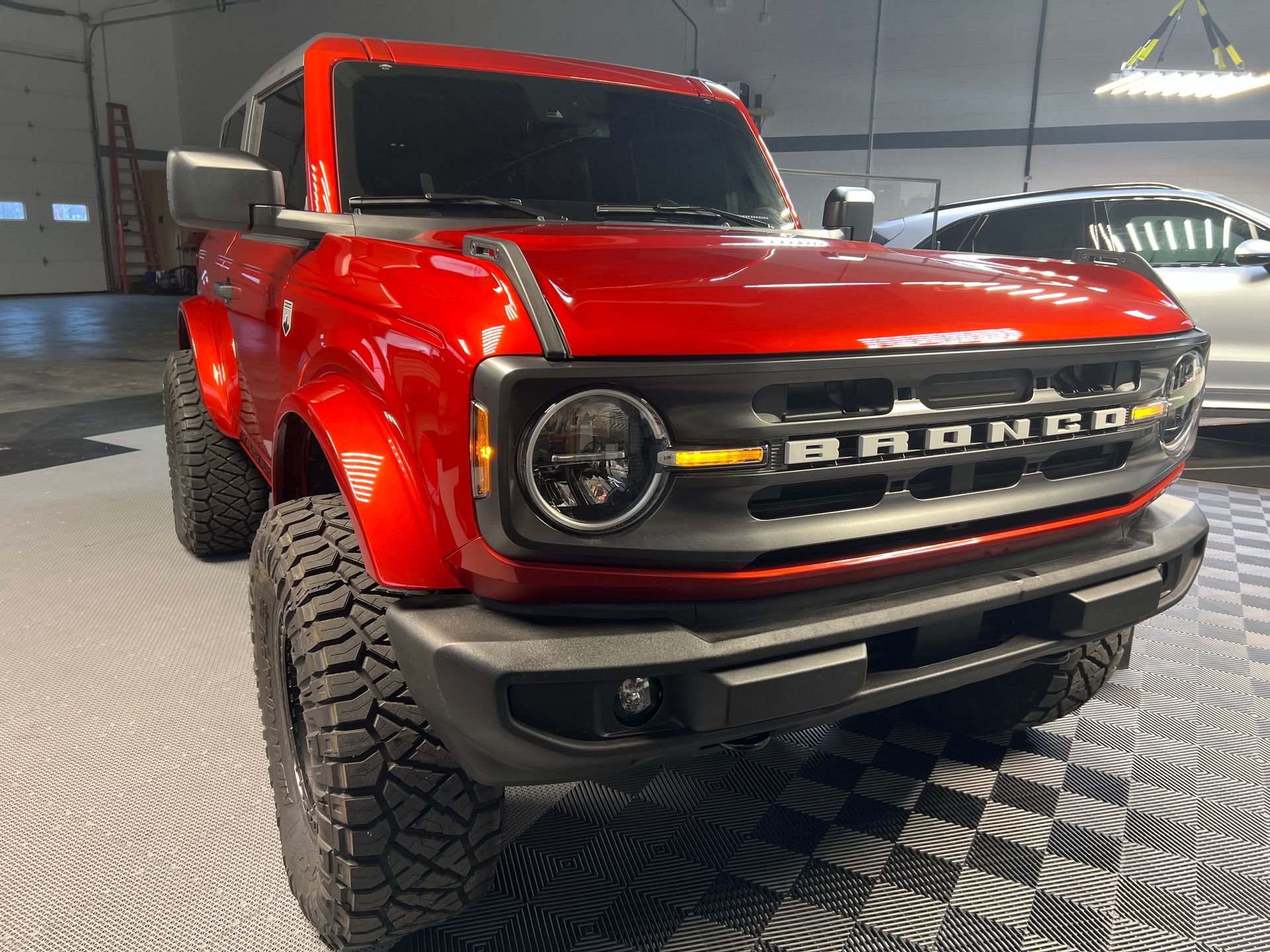 Red Ford Bronco SUV, parked inside a garage, angled view. Black grill and off-road tires.