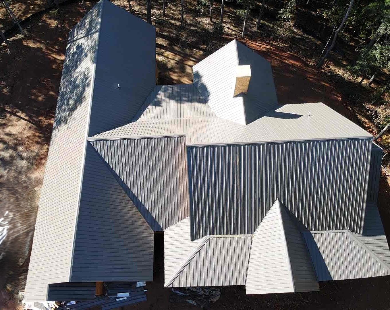 Overhead view of a modern house with a complex multi-faceted gray metal roof in a wooded area.