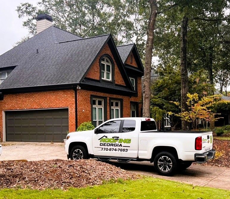 White truck with roofing company logo parked in front of a brick house with a new black roof.