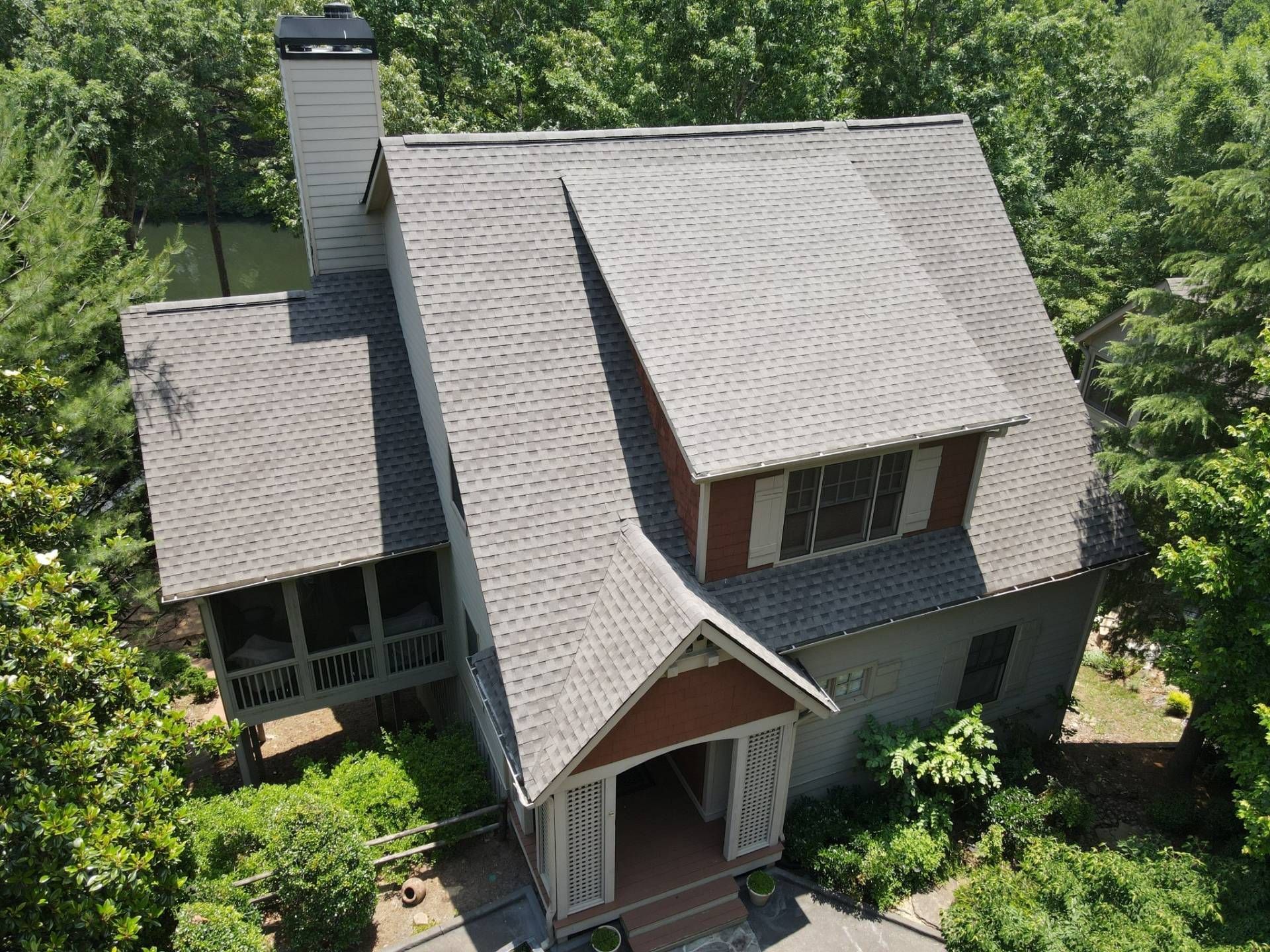 Gray house with multiple roof angles, surrounded by green trees.
