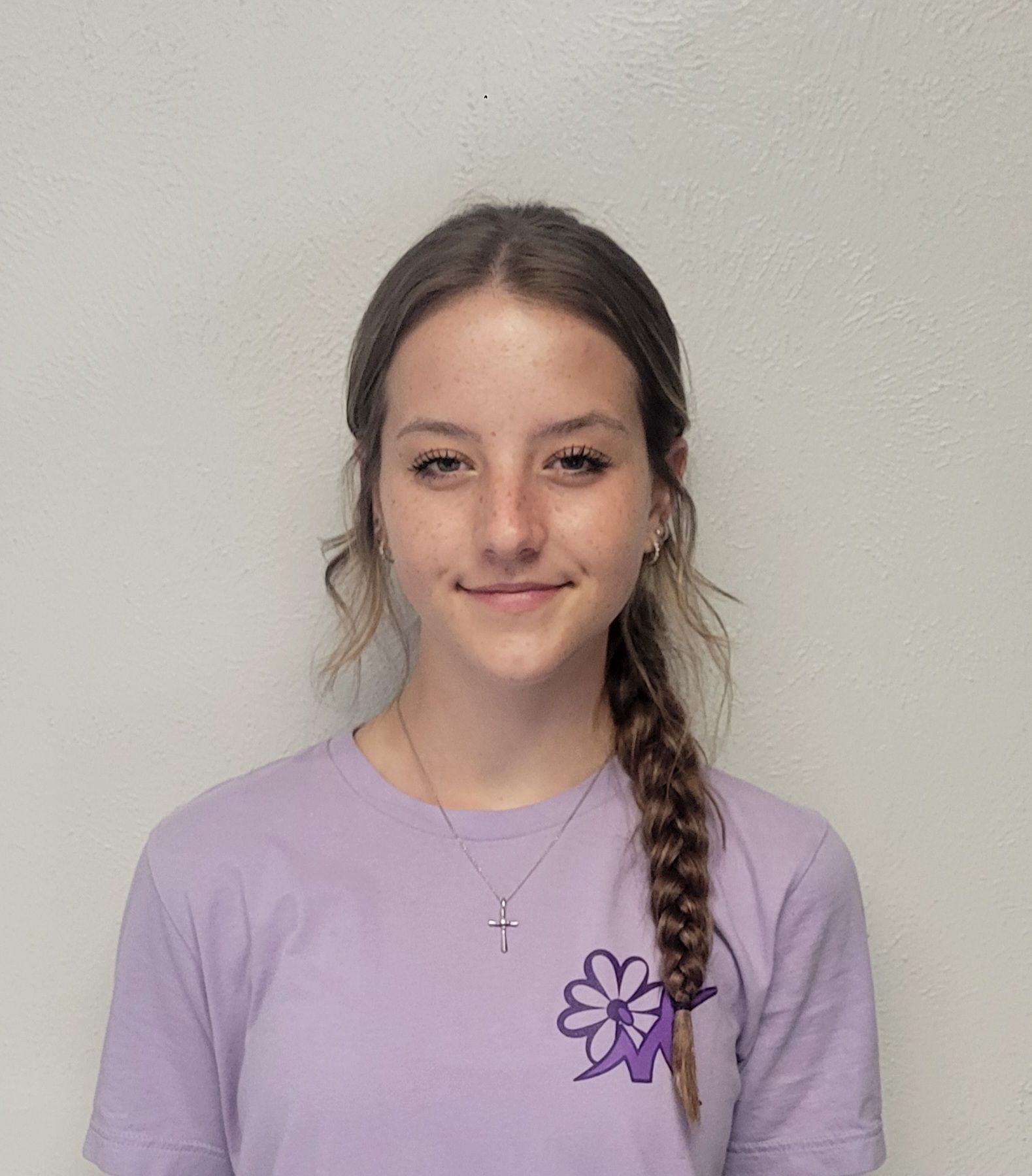 Woman with brown hair in a braid wearing a purple shirt, smiling, in front of a white wall.