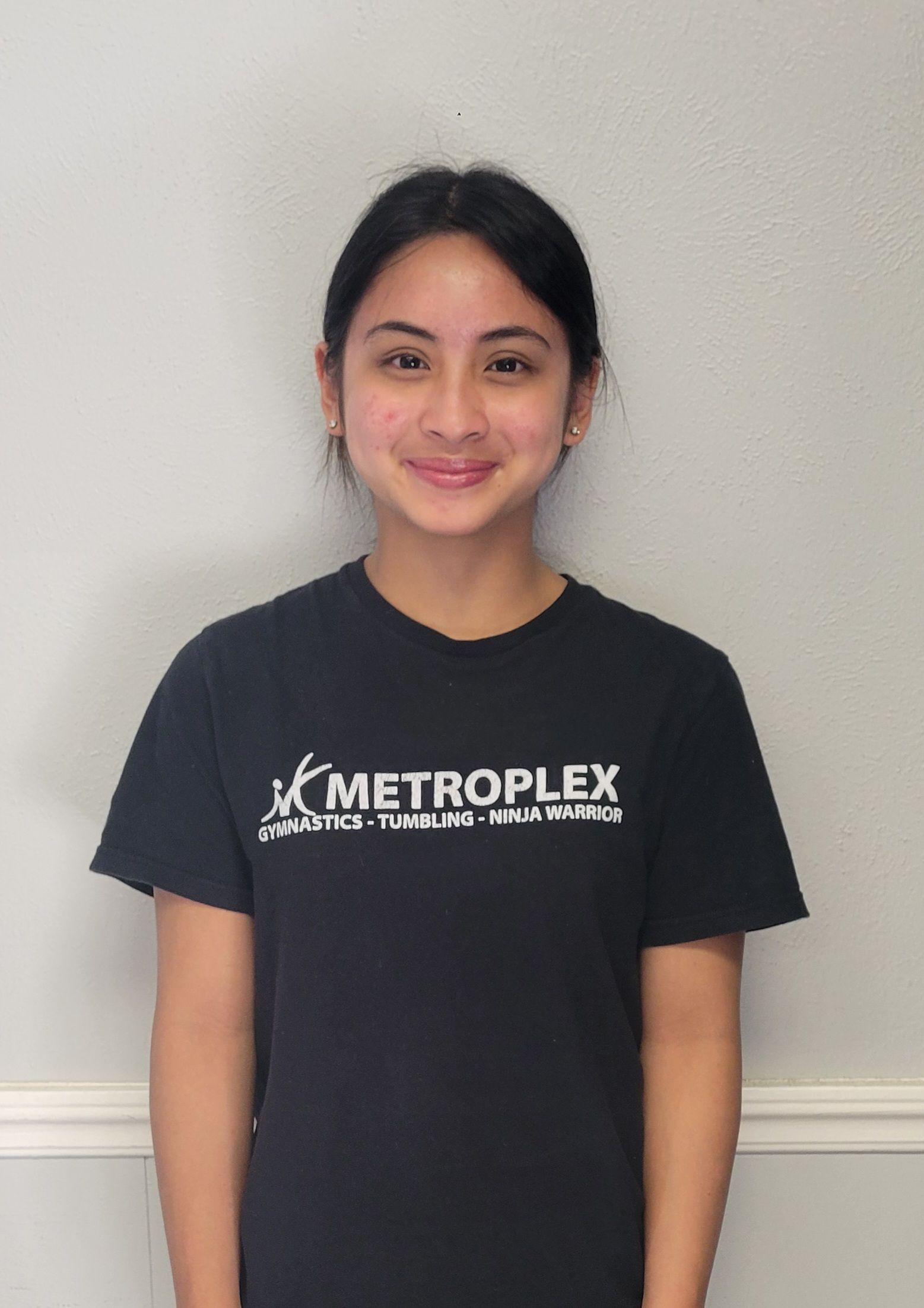 Woman wearing a black t-shirt, smiling, standing in front of a white wall.