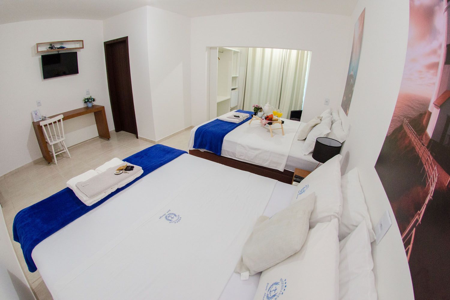 Um quarto de hotel com duas camas, uma escrivaninha e uma televisão.