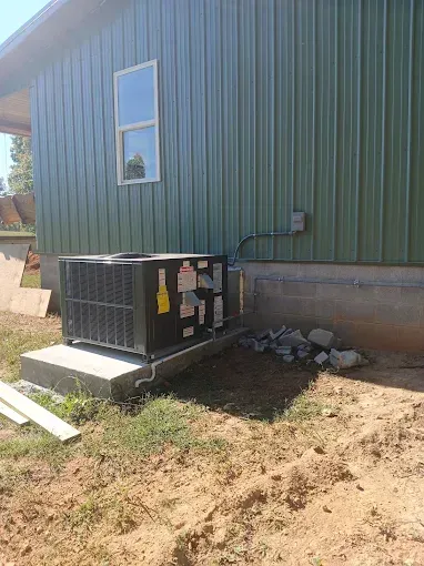 Outdoor HVAC unit beside a green metal building with a window and dirt ground