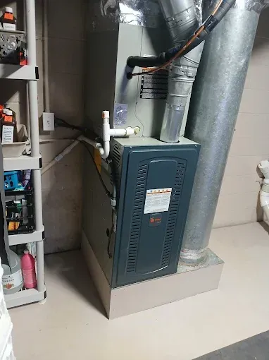 Basement furnace with metal ductwork and pipes beside a utility cabinet
