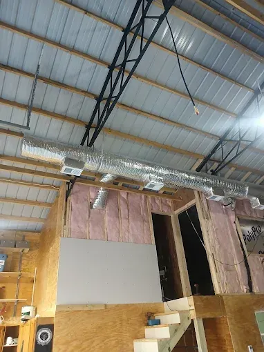 Interior of a warehouse with exposed ceiling beams, pink insulation, and a partially built loft area.