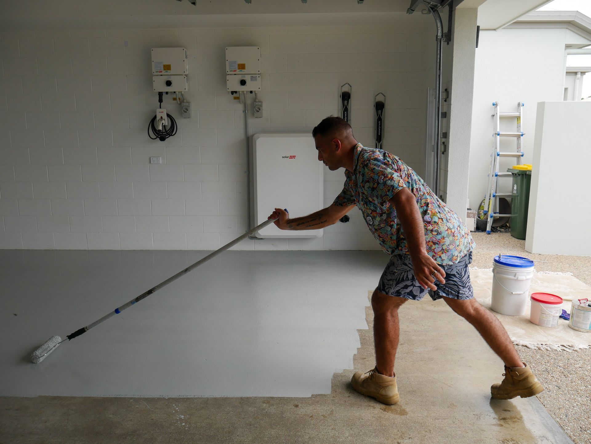 A man is painting a garage floor with a roller.